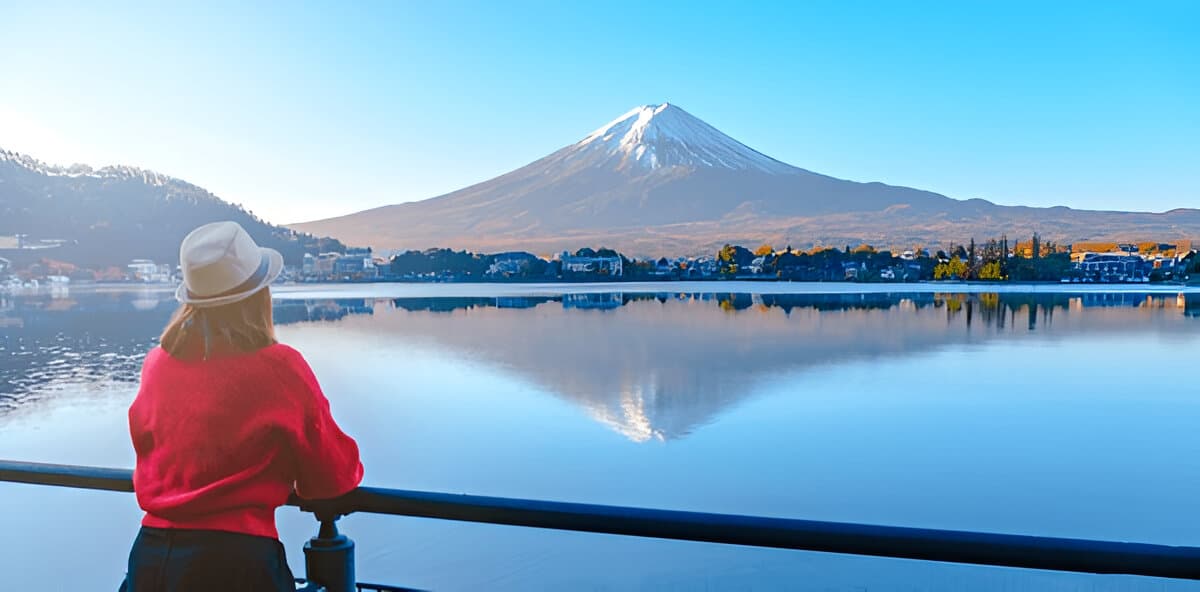 Mount Fuji reflected in Lake Kawaguchi with a person in a red sweater.